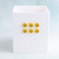 White pen holder snappy pot with little yellow smiley face charm on charms