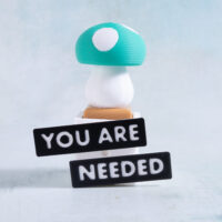 Green mushroom clicker fidget on a white Snappy Pots planter with you are needed word charms